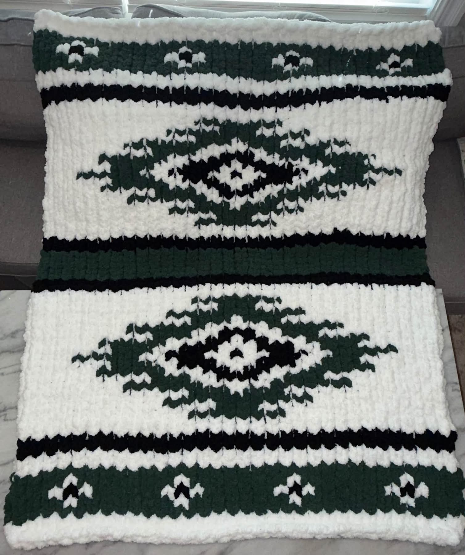 Hand-knit green, black, and white patterned blanket by Rustic Home Creations